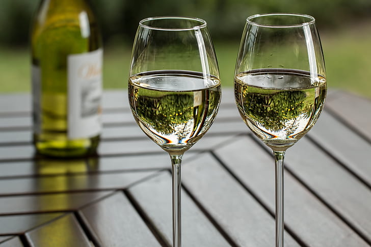 A glass of crisp white wine in a vineyard setting — Pinot Grigio and Pinot Gris are made from the same grape but taste completely different depending on where and how they are made