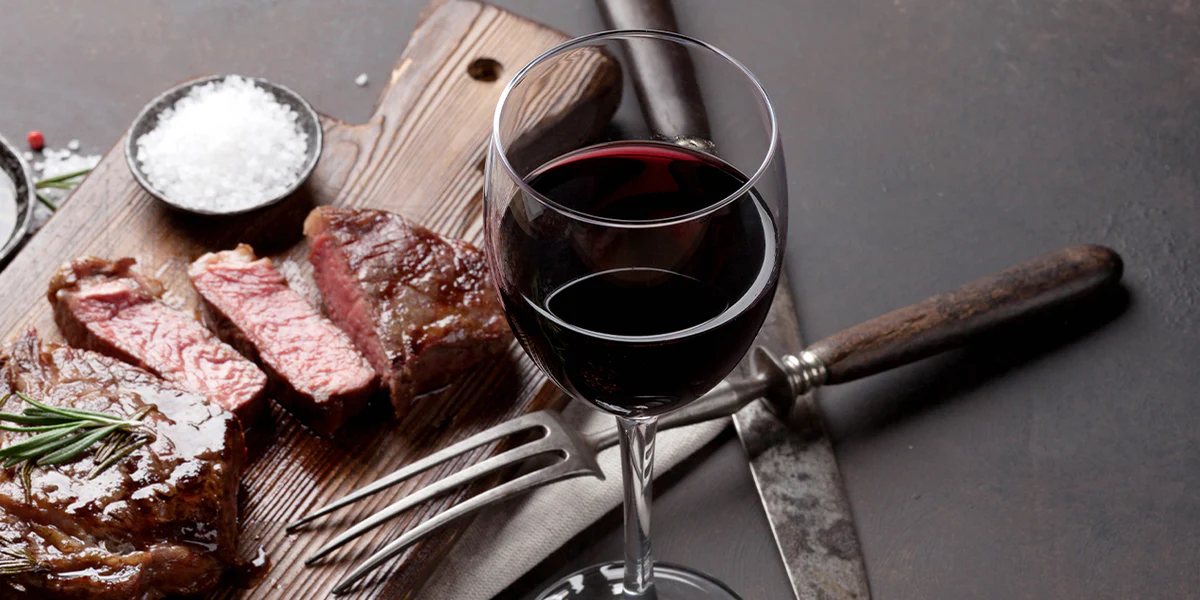 A glass of red wine beside a steak dinner — the classic Malbec pairing