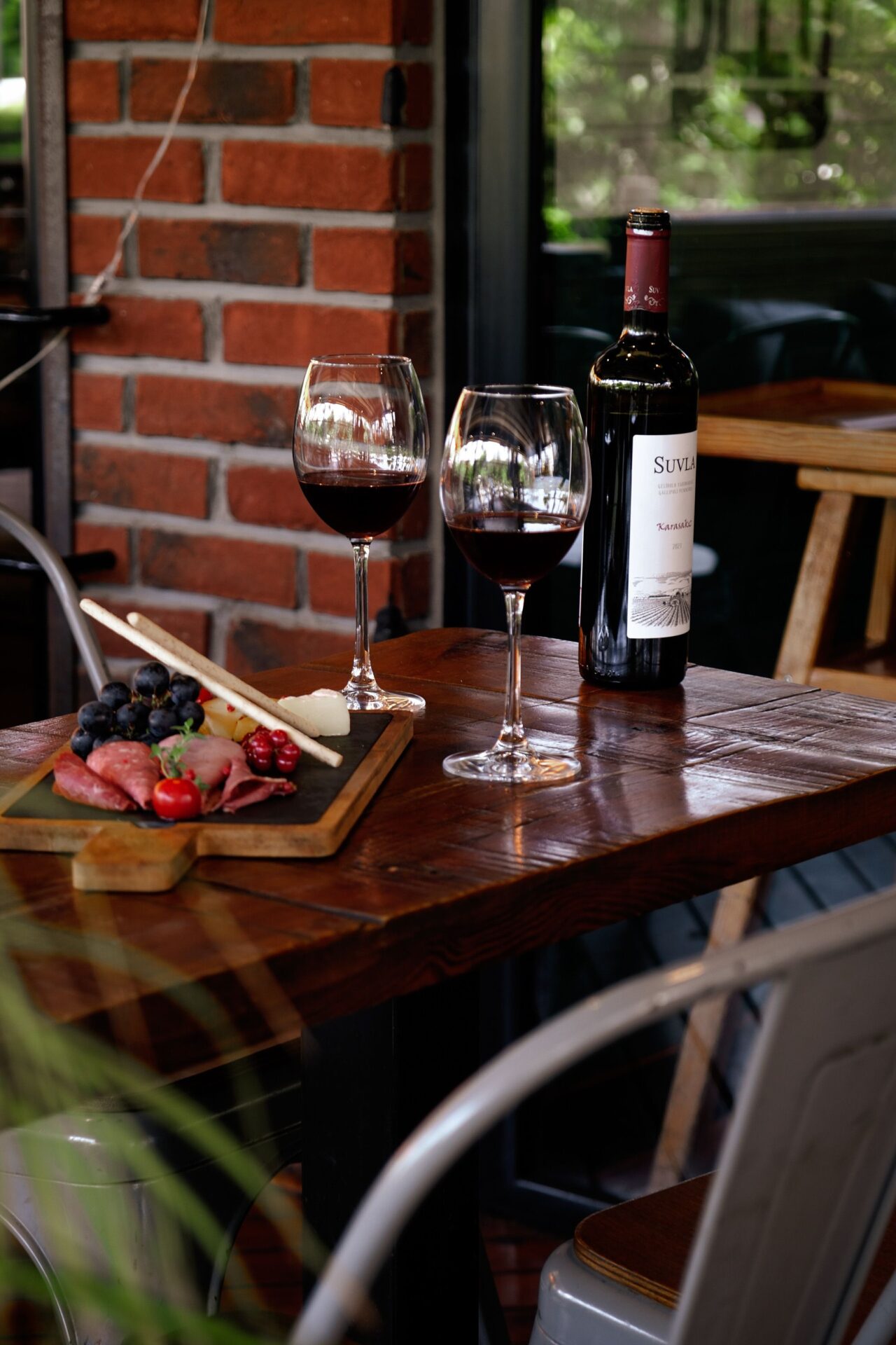 A glass of red wine with a charcuterie board including cured ham