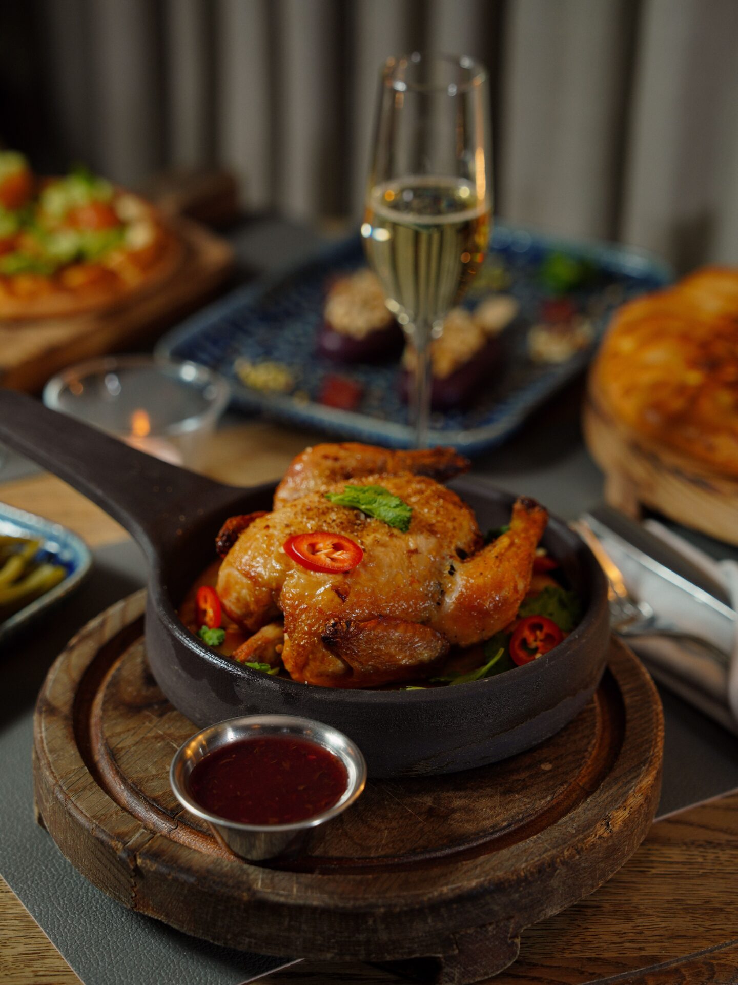 A whole roasted chicken served with sauce alongside a glass of wine