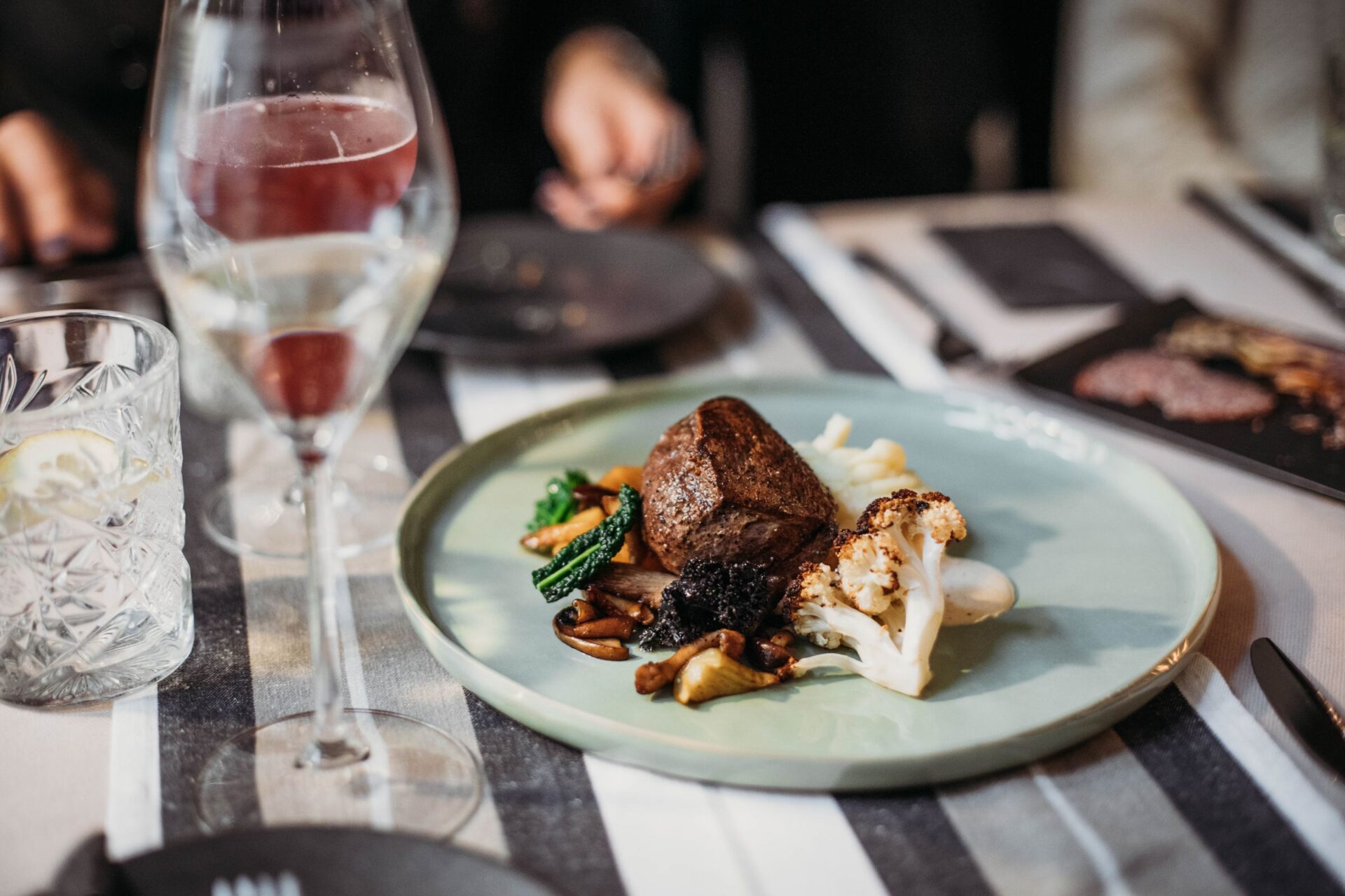 A grilled steak with mushrooms and cauliflower on a dark plate beside a glass of red wine