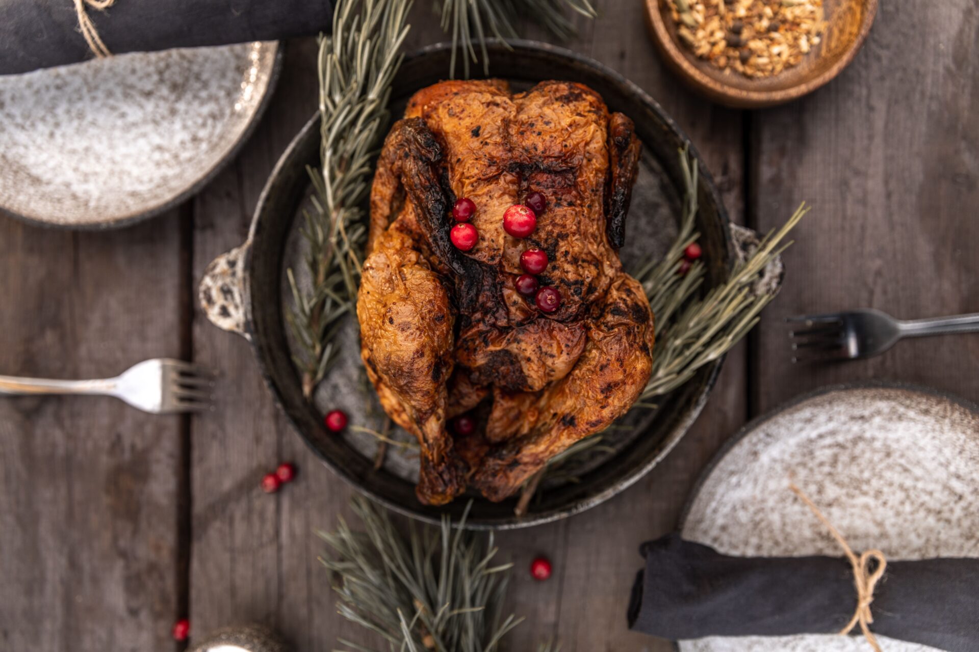 A whole roasted turkey garnished with fresh cranberries and rosemary on a rustic wooden table