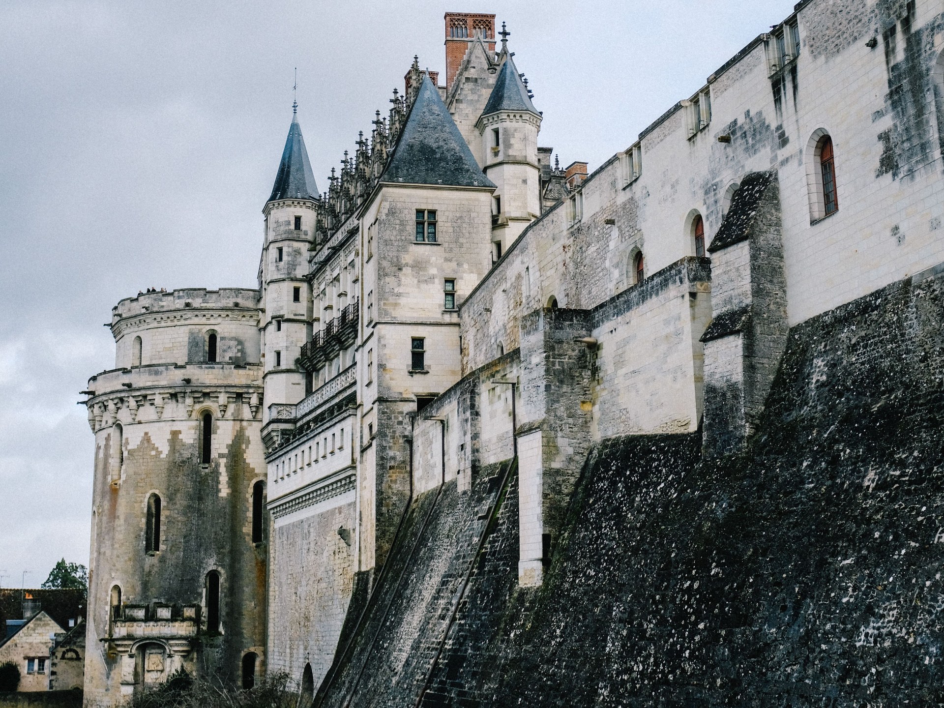 Pale limestone towers with slate-capped turrets and a high stone rampart of the Château d'Amboise under a grey sky